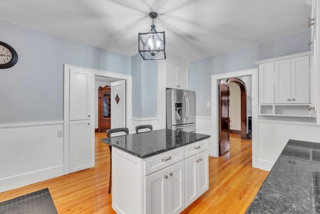 kitchen featuring stainless steel fridge, dark stone counters, pendant lighting, light hardwood / wood-style floors, and white cabinetry