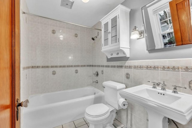 full bathroom featuring tile patterned flooring, tiled shower / bath combo, toilet, and tile walls