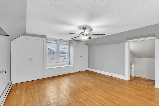 additional living space with a textured ceiling, light hardwood / wood-style flooring, baseboard heating, and lofted ceiling