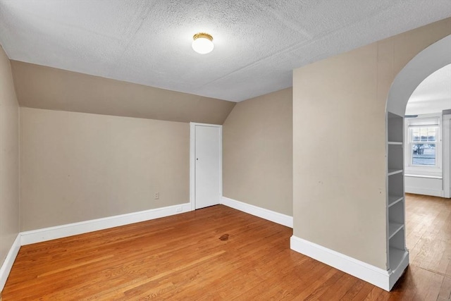 additional living space featuring wood-type flooring, a textured ceiling, and vaulted ceiling