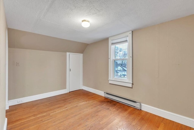 bonus room featuring baseboard heating, a textured ceiling, vaulted ceiling, and light wood-type flooring