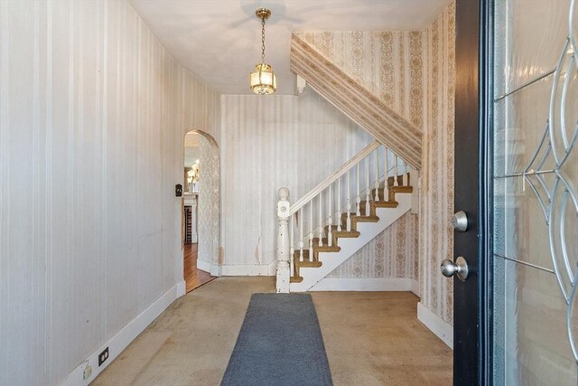 foyer entrance with stairs, arched walkways, wallpapered walls, and baseboards