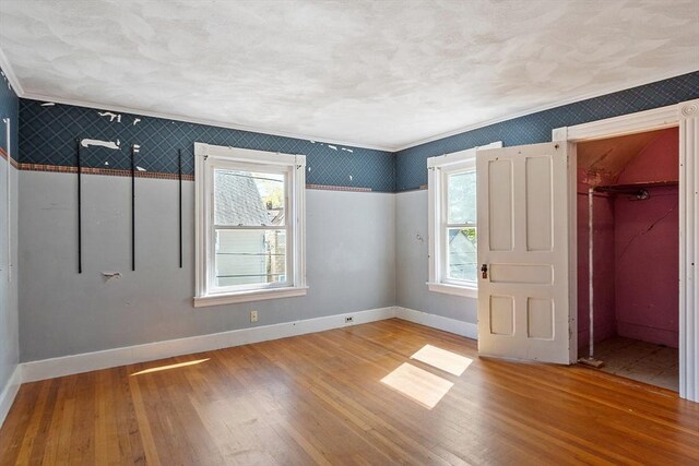 unfurnished bedroom with baseboards, wallpapered walls, multiple windows, and wood finished floors