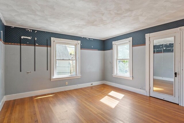 unfurnished room with plenty of natural light, wood finished floors, and wallpapered walls