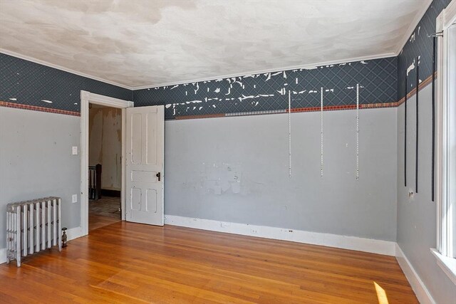 unfurnished room featuring baseboards, radiator heating unit, and wood finished floors