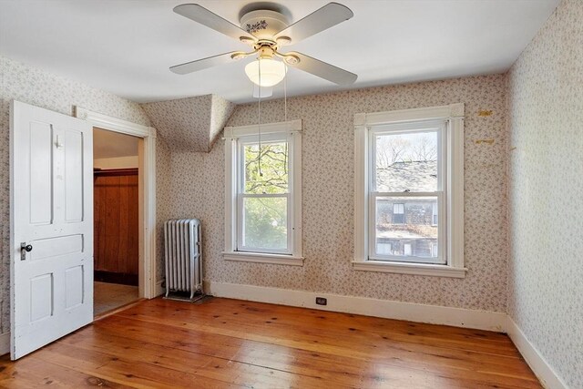 bonus room with radiator heating unit, a ceiling fan, wallpapered walls, and light wood-style flooring