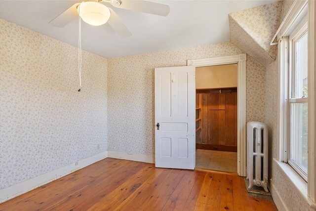 unfurnished bedroom featuring hardwood / wood-style flooring, multiple windows, wallpapered walls, and radiator