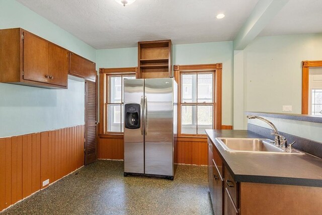kitchen with brown cabinets, dark countertops, a sink, a wainscoted wall, and stainless steel refrigerator with ice dispenser
