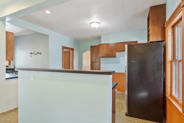 kitchen featuring freestanding refrigerator, recessed lighting, brown cabinetry, and light carpet