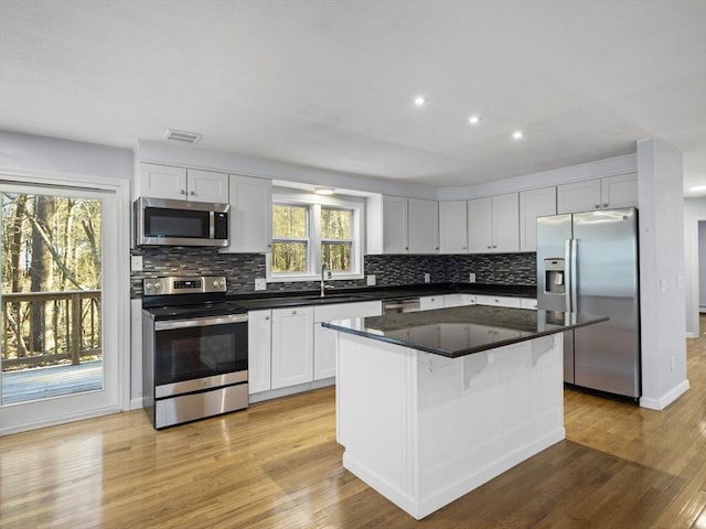 kitchen featuring appliances with stainless steel finishes, decorative backsplash, light wood-type flooring, and visible vents