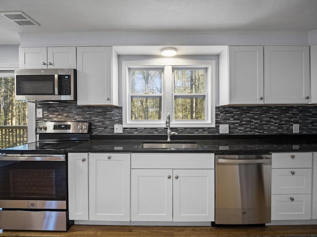kitchen with appliances with stainless steel finishes, a sink, white cabinetry, backsplash, and visible vents