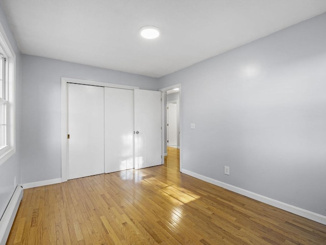 unfurnished bedroom with baseboards, light wood-style flooring, baseboard heating, and a closet