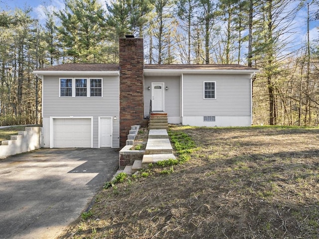 view of front facade featuring an attached garage, a chimney, entry steps, and aphalt driveway