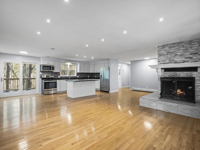 unfurnished living room with a fireplace, a sink, baseboards, light wood finished floors, and recessed lighting