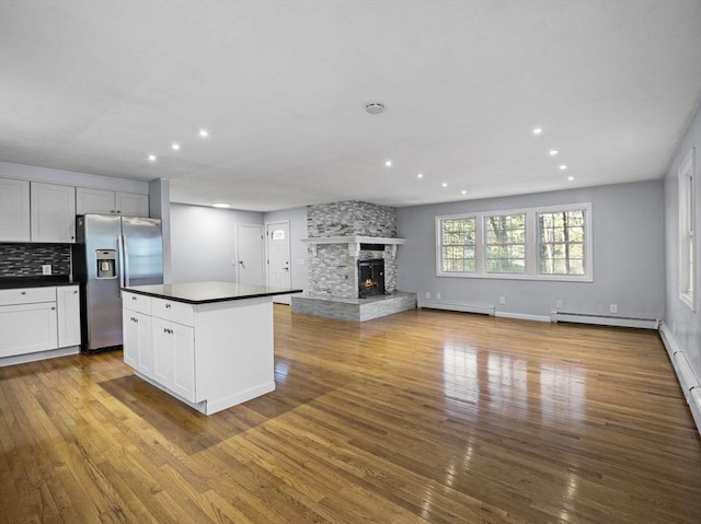 kitchen with dark countertops, stainless steel fridge, a stone fireplace, wood finished floors, and a baseboard heating unit