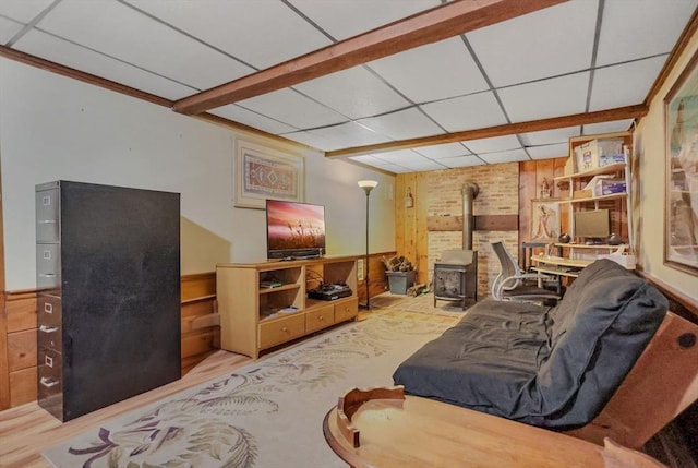 living room with a wood stove, a drop ceiling, wooden walls, and light hardwood / wood-style flooring