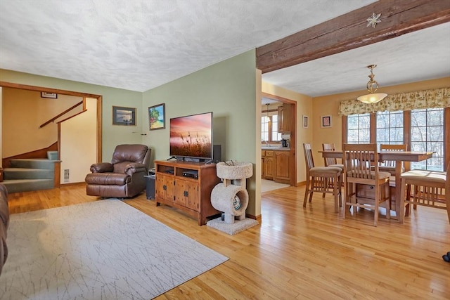 living room featuring beam ceiling, light hardwood / wood-style flooring, and a textured ceiling