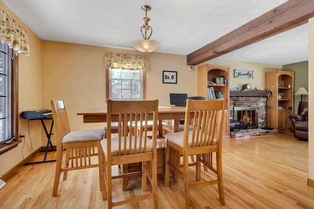 dining space featuring beam ceiling, light hardwood / wood-style floors, and a brick fireplace