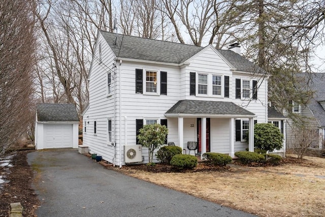 colonial-style house with a shingled roof, a chimney, a porch, and an outdoor structure