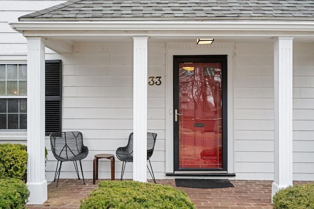 entrance to property with covered porch and roof with shingles