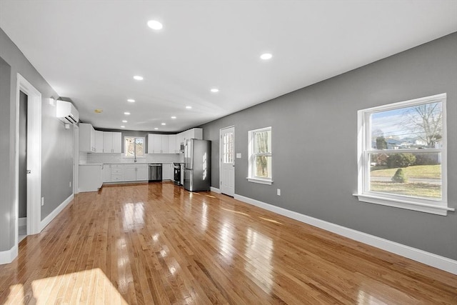 unfurnished living room with light hardwood / wood-style flooring, a wall mounted air conditioner, plenty of natural light, and sink