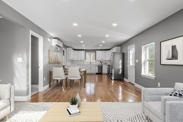 living room with a wall mounted air conditioner, a wealth of natural light, and wood-type flooring