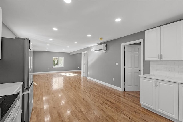 kitchen with stainless steel fridge, light stone countertops, a wall mounted AC, and white cabinets