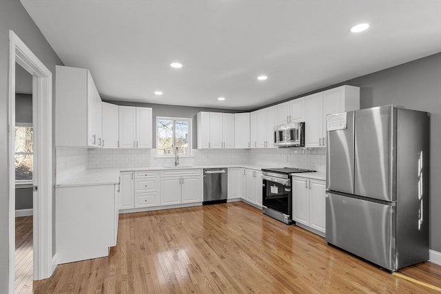 kitchen with appliances with stainless steel finishes, sink, light hardwood / wood-style flooring, and white cabinets