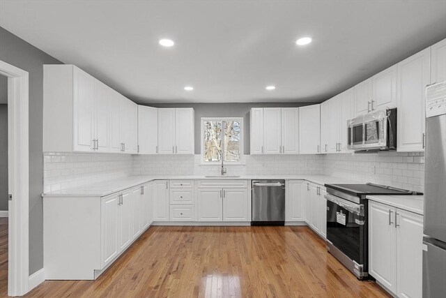 kitchen with tasteful backsplash, sink, white cabinets, light hardwood / wood-style floors, and stainless steel appliances