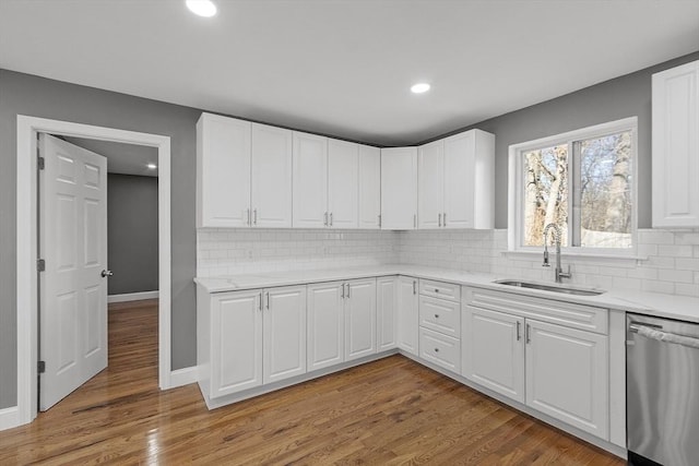 kitchen with tasteful backsplash, white cabinetry, dishwasher, sink, and light wood-type flooring