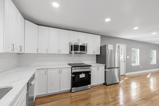 kitchen featuring appliances with stainless steel finishes, white cabinetry, tasteful backsplash, light stone countertops, and light wood-type flooring