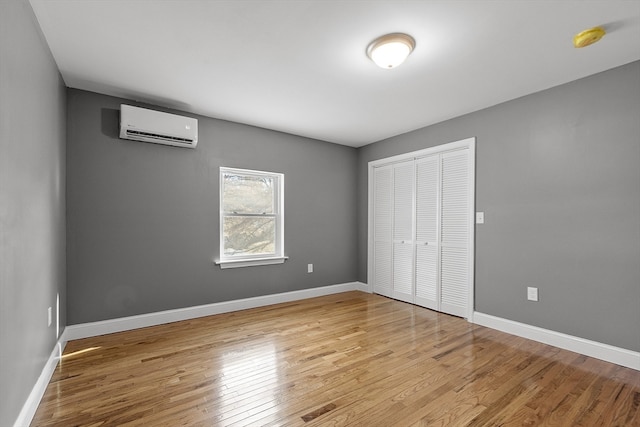 unfurnished bedroom featuring a wall mounted air conditioner, light wood-type flooring, and a closet