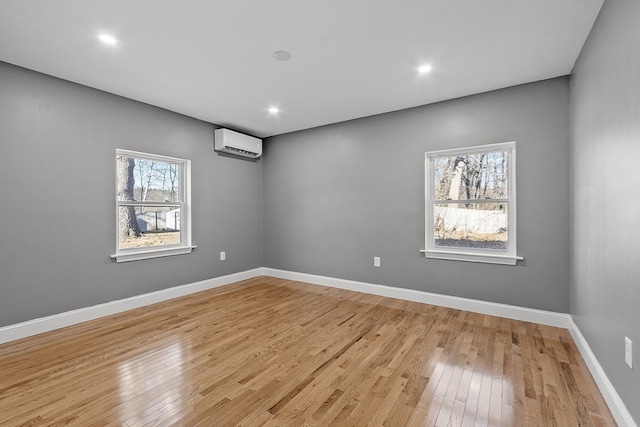 empty room featuring a wealth of natural light, light hardwood / wood-style floors, and an AC wall unit