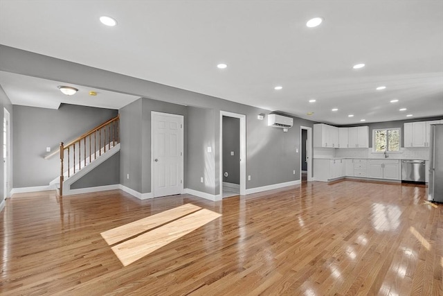 unfurnished living room featuring a wall mounted AC and light hardwood / wood-style floors