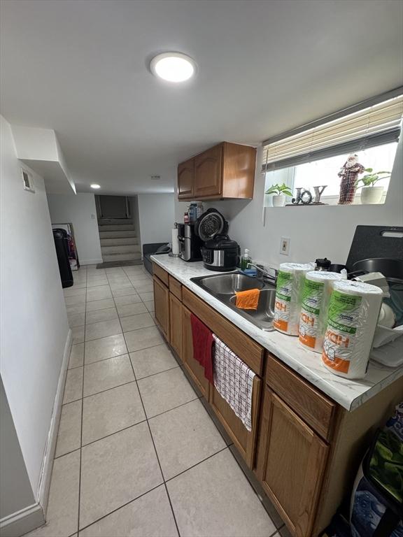 kitchen with brown cabinets, light countertops, light tile patterned flooring, a sink, and baseboards