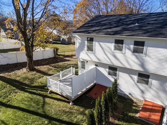view of side of home featuring a deck, fence, a shingled roof, and a lawn