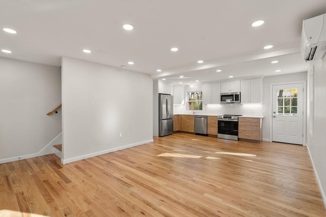 kitchen with a wall mounted AC, stainless steel appliances, light wood-style flooring, baseboards, and white cabinets