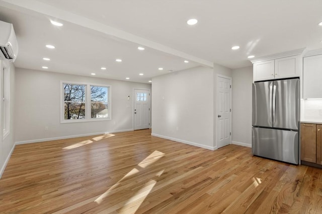 unfurnished living room featuring light wood-type flooring, recessed lighting, a wall mounted AC, and baseboards