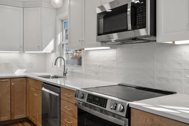 kitchen with decorative backsplash, stainless steel appliances, light countertops, a sink, and white cabinetry