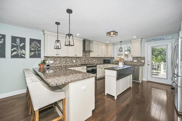 1 Woodland Ct Unit B, Milford, MA 01757 - kitchen featuring wall chimney range hood, appliances with stainless steel finishes, a peninsula, tasteful backsplash, and dark wood-style flooring