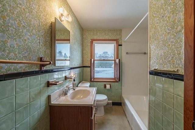 bathroom with a wainscoted wall, tile walls, toilet, and wallpapered walls