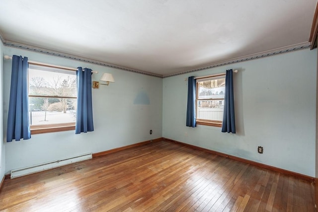 empty room featuring a baseboard heating unit, baseboards, and hardwood / wood-style flooring