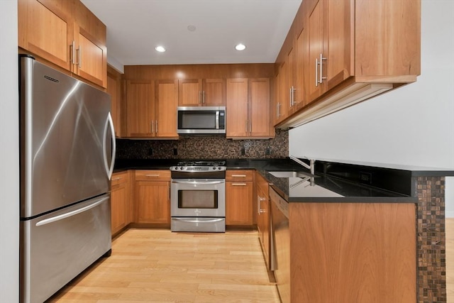 kitchen featuring stainless steel appliances, dark stone countertops, decorative backsplash, sink, and light wood-type flooring