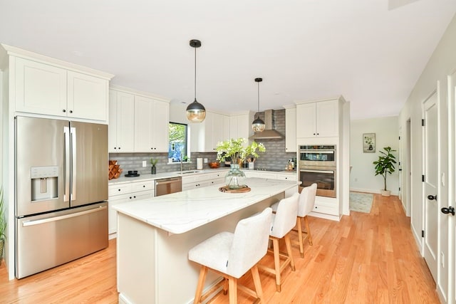 kitchen with stainless steel appliances, light wood-type flooring, a kitchen island, tasteful backsplash, and wall chimney range hood