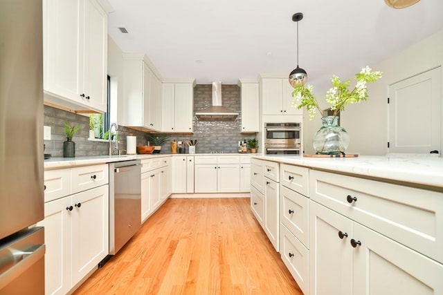 kitchen with tasteful backsplash, appliances with stainless steel finishes, light hardwood / wood-style floors, wall chimney range hood, and decorative light fixtures