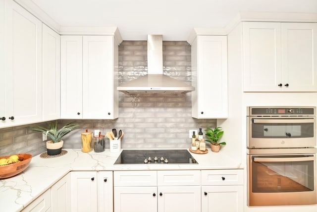 kitchen featuring stainless steel double oven, white cabinetry, decorative backsplash, wall chimney range hood, and black electric stovetop