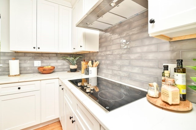 kitchen featuring tasteful backsplash, white cabinetry, wall chimney exhaust hood, and black electric cooktop