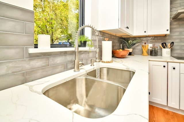 room details with white cabinets, light stone countertops, backsplash, sink, and light hardwood / wood-style floors