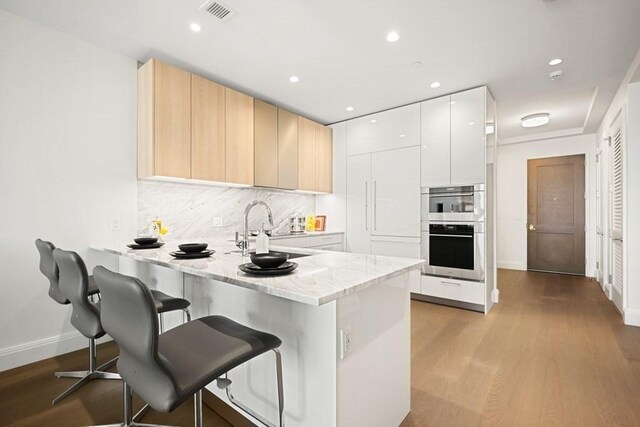 240 Devonshire St Unit 4003, Boston, MA 02110 - kitchen with double oven, a peninsula, modern cabinets, a kitchen bar, and wood finished floors