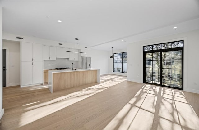 kitchen with decorative light fixtures, a center island with sink, stainless steel refrigerator with ice dispenser, light wood-type flooring, and white cabinets